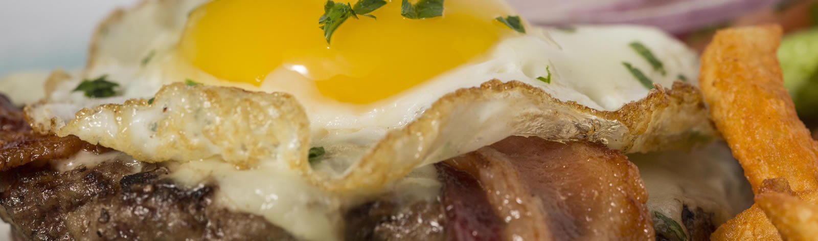 Breakfast burger topped with a fried egg and bacon, served with fries