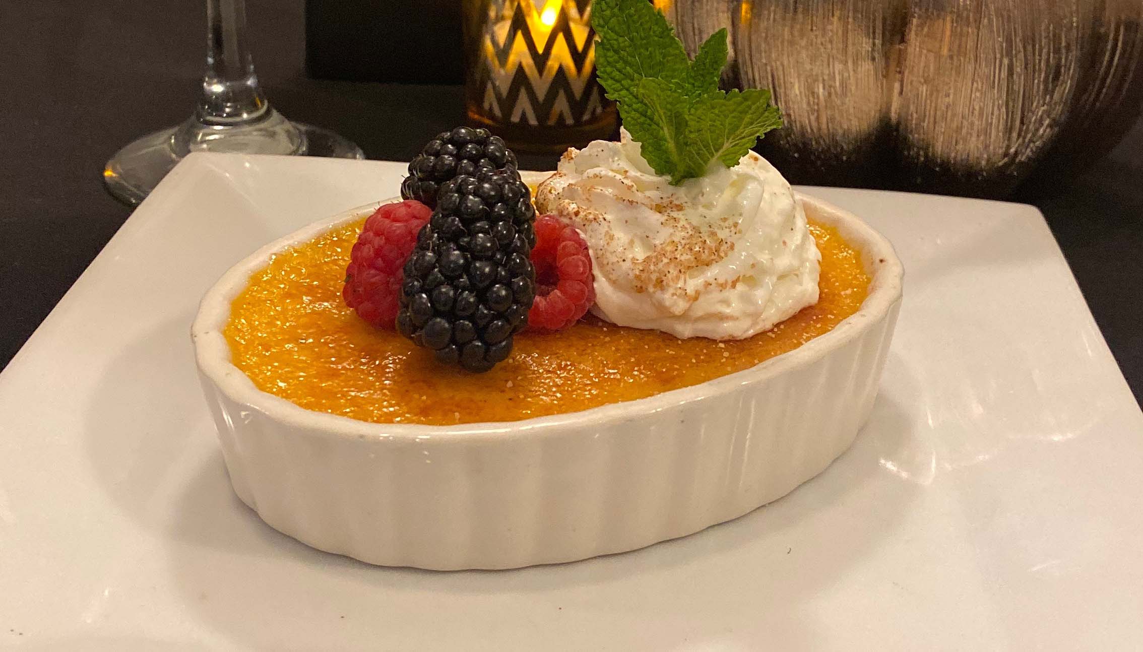 Creme brulee topped with berries, mint and whipped cream