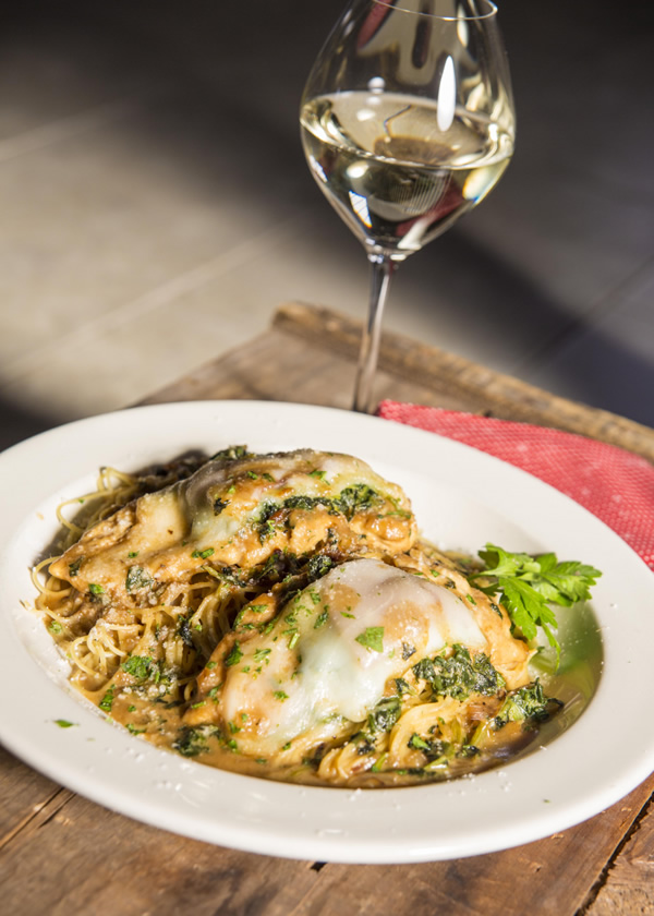 Chicken topped with melted cheese over pasta with a glass of white wine