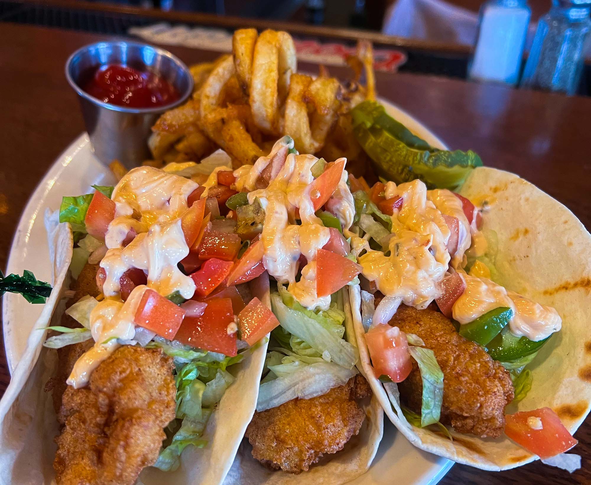 Three fried haddock fish tacos served with curly fries